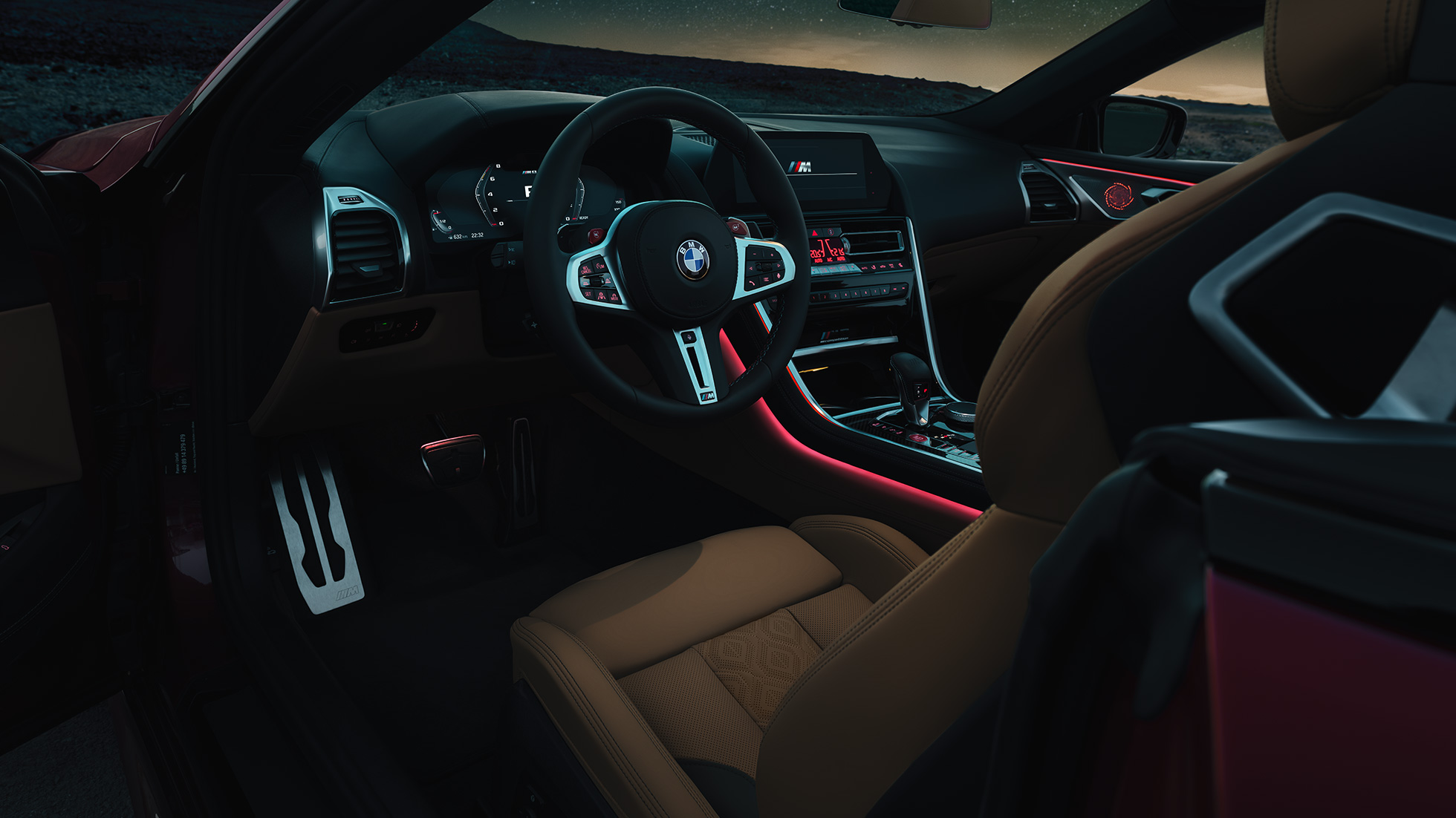 BMW M8 Competition Cabrio, cockpit. BMW M8 Competition Cabrio, cockpit à noite, com o volante M em pele e a luz ambiente em vermelho.