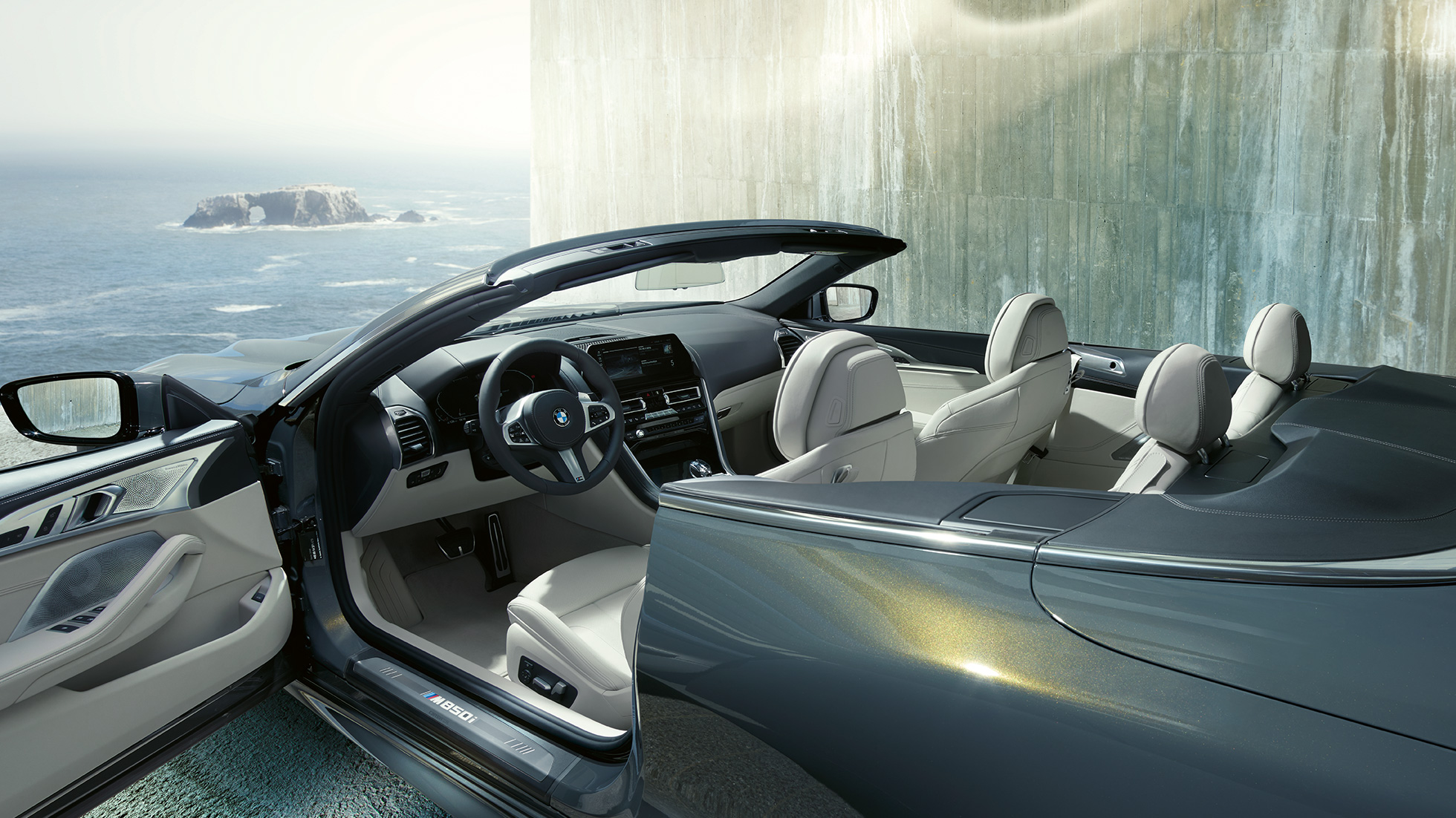 BMW M850i xDrive Cabrio, interior. BMW M850i xDrive Cabrio em cinza Dravit metalizada com capota flexível aberta, interior com volante M em pele e estofos em pele Merino BMW Individual em branco Ivory.