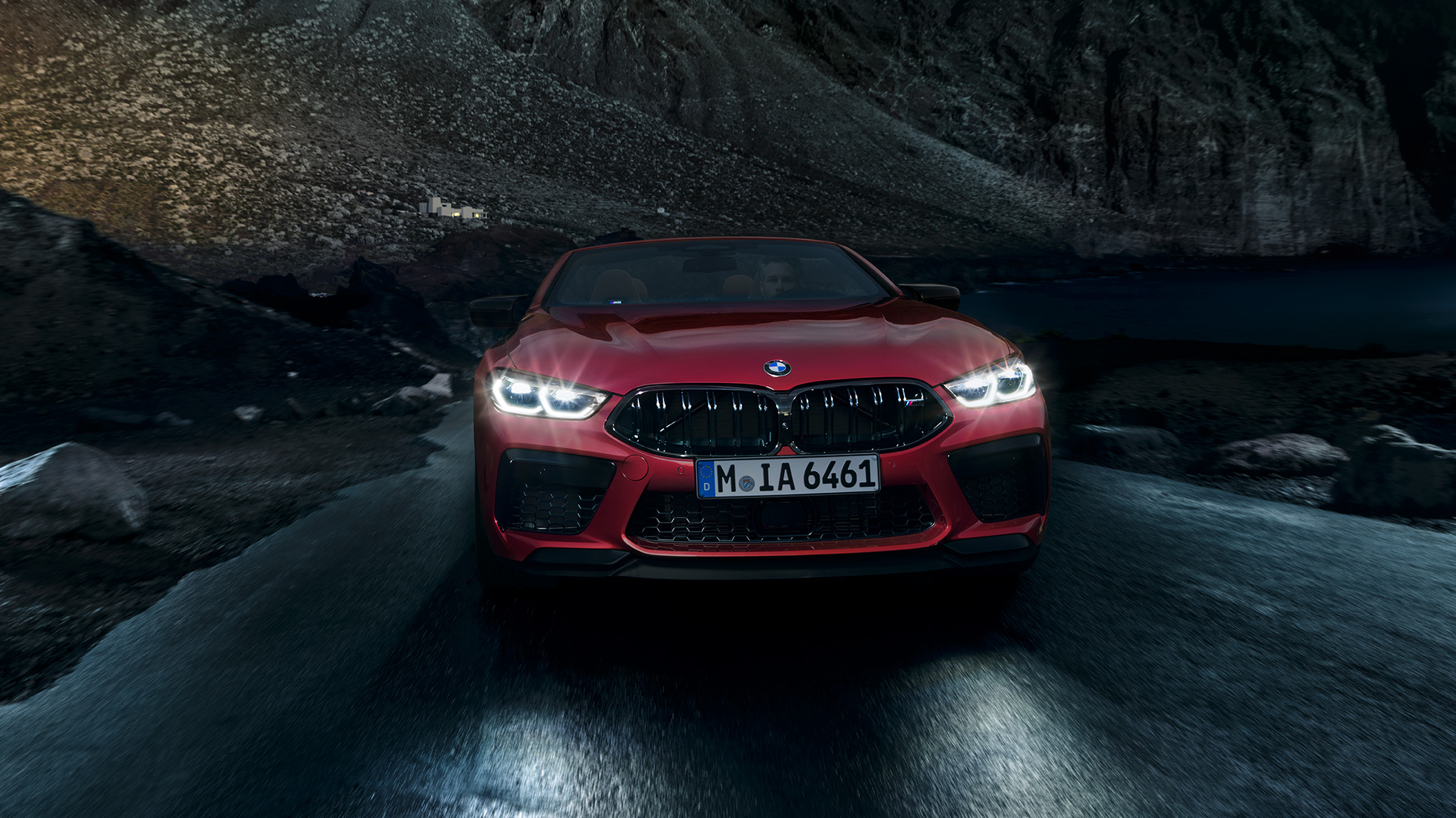 BMW M8 Competition Cabrio, perspetiva frontal. BMW M8 Competition Cabrio na pintura vermelho Motegi metalizada com faróis ligados, em movimento, à noite, perspetiva frontal.