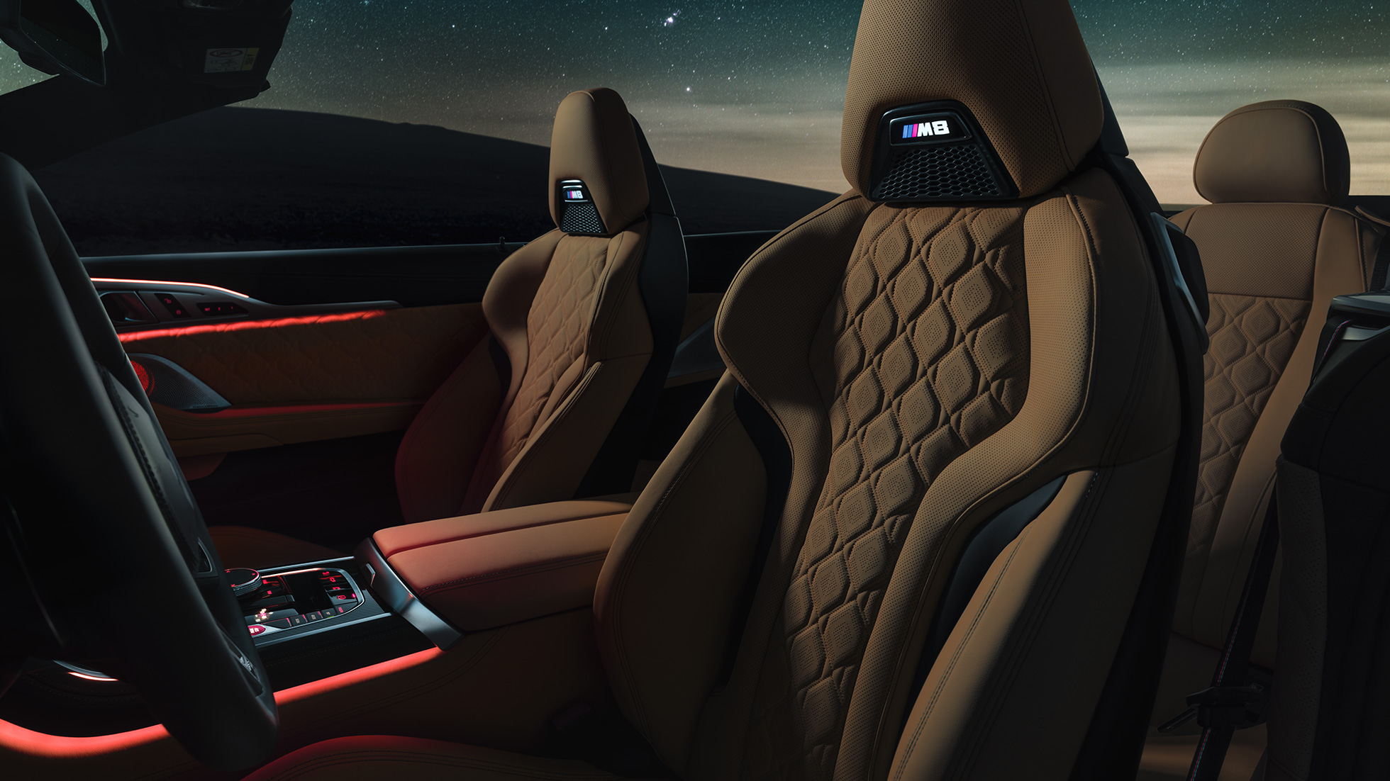 Bancos desportivos M em pele Merino. BMW M8 Competition Cabrio com capota flexível aberta sob um céu estrelado, interior com bancos desportivos M em pele Merino e luz ambiente em vermelho.