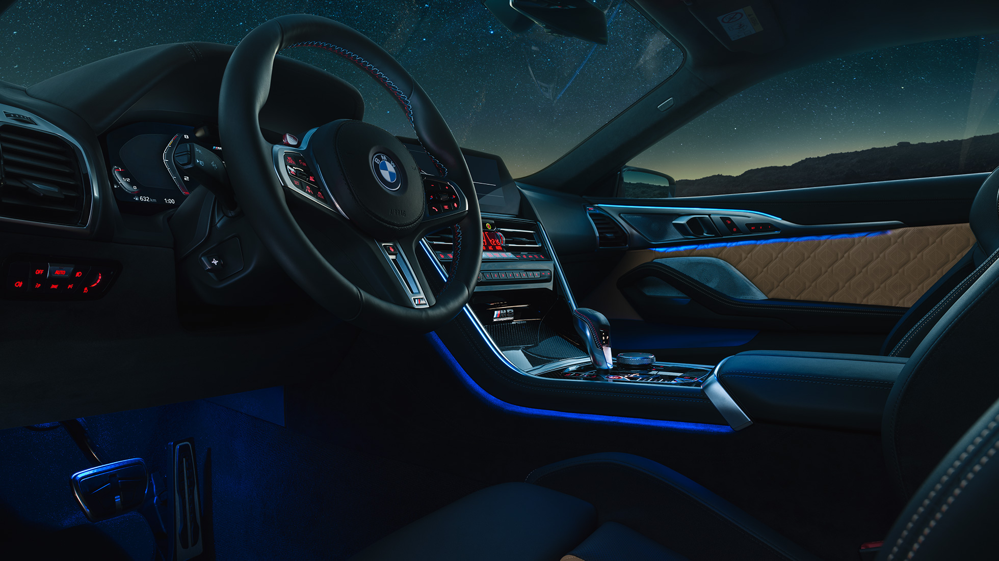 BMW M8 Competition Coupé, posto de condução. BMW M8 Competition Coupé, posto de condução à noite, com volante M em pele e luz ambiente em azul.