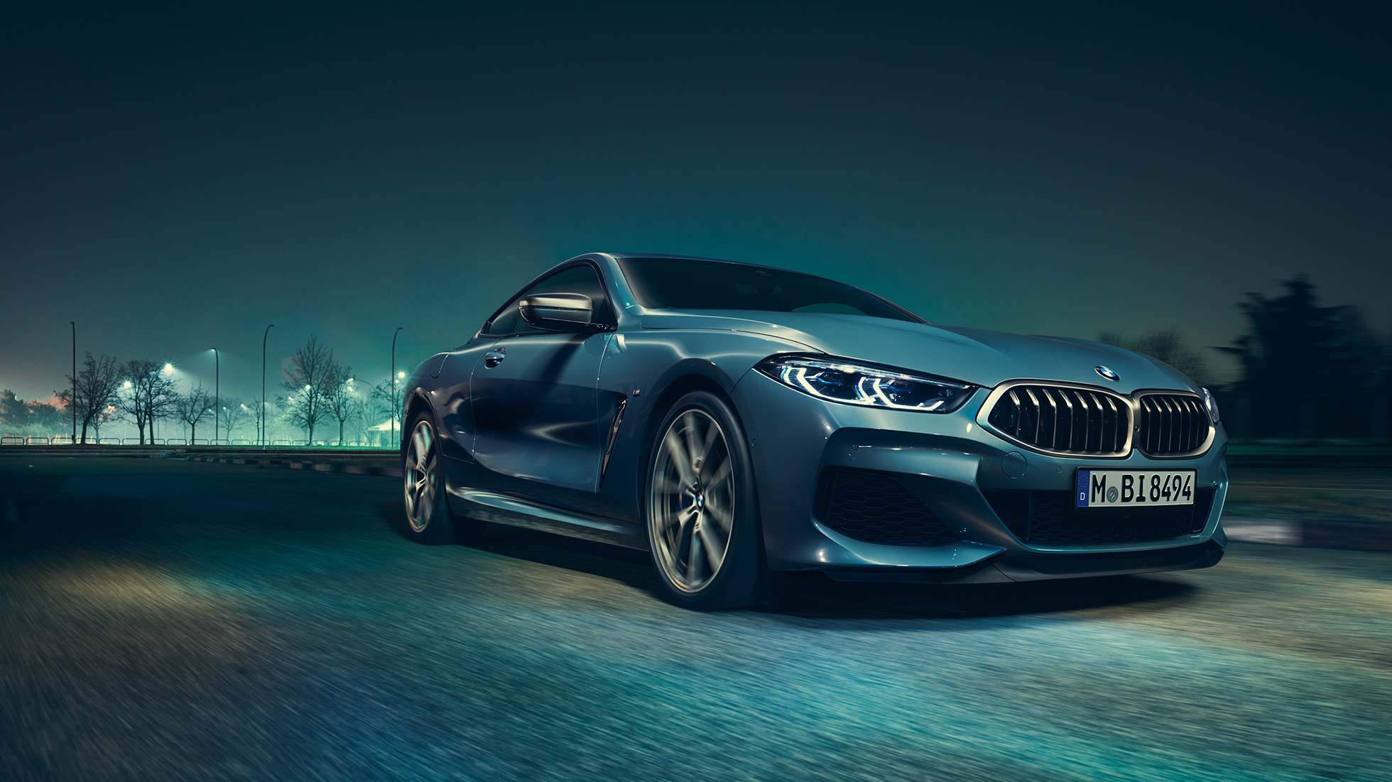 BMW M850i xDrive Coupé, perspetiva frontal esquerda a três quartos. BMW M850i xDrive Coupé na pintura azul Barcelona metalizada, em movimento à noite, perspetiva frontal esquerda a três quartos.