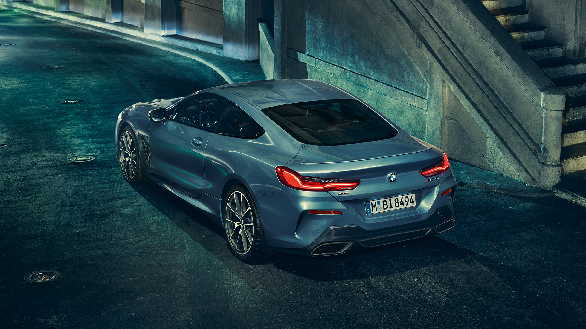 BMW M850i xDrive Coupé, perspetiva traseira esquerda a três quartos. BMW M850i xDrive Coupé na pintura azul Barcelona metalizada, parado à noite, perspetiva traseira esquerda a três quartos.