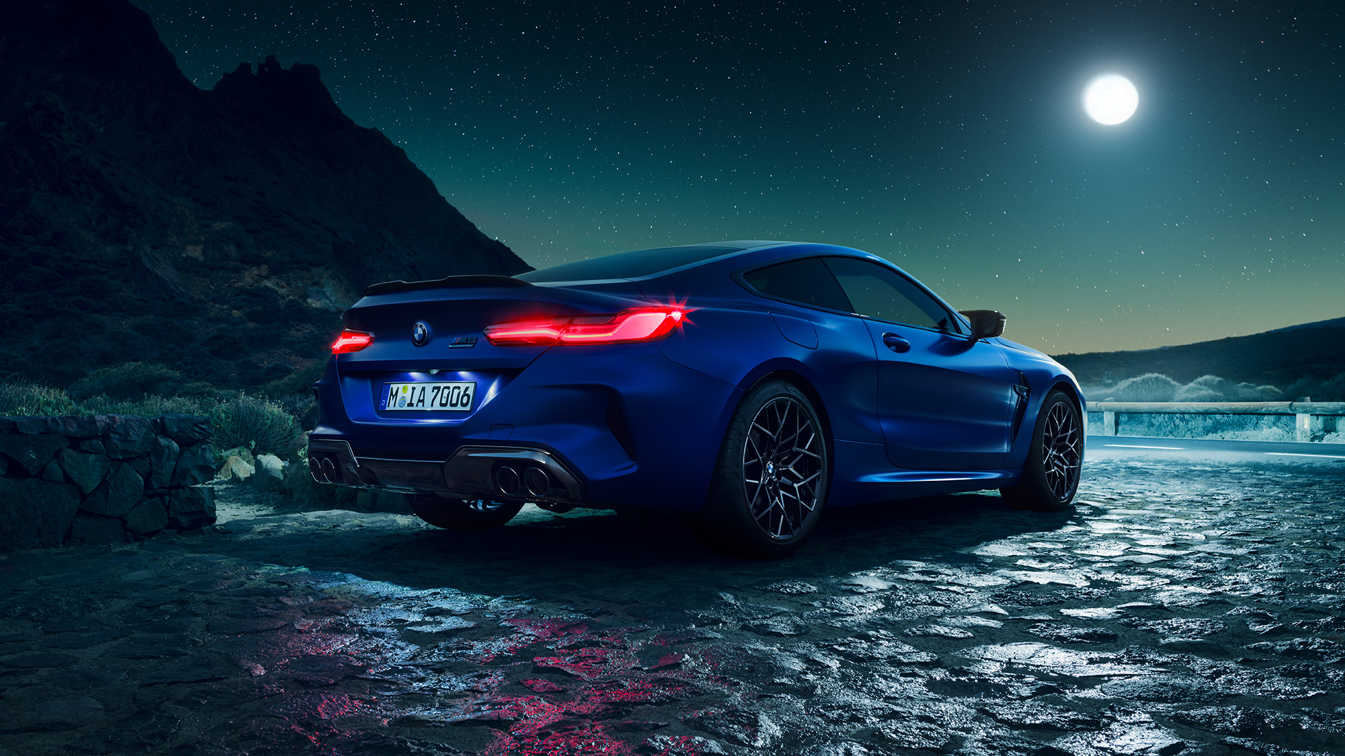 BMW M8 Competition Coupé, perspetiva traseira a três quartos. BMW M8 Competition Coupé na pintura azul Marina Bay metalizada com faróis traseiros LED iluminados, parado num cenário de lua cheia, perspetiva traseira a três quartos.