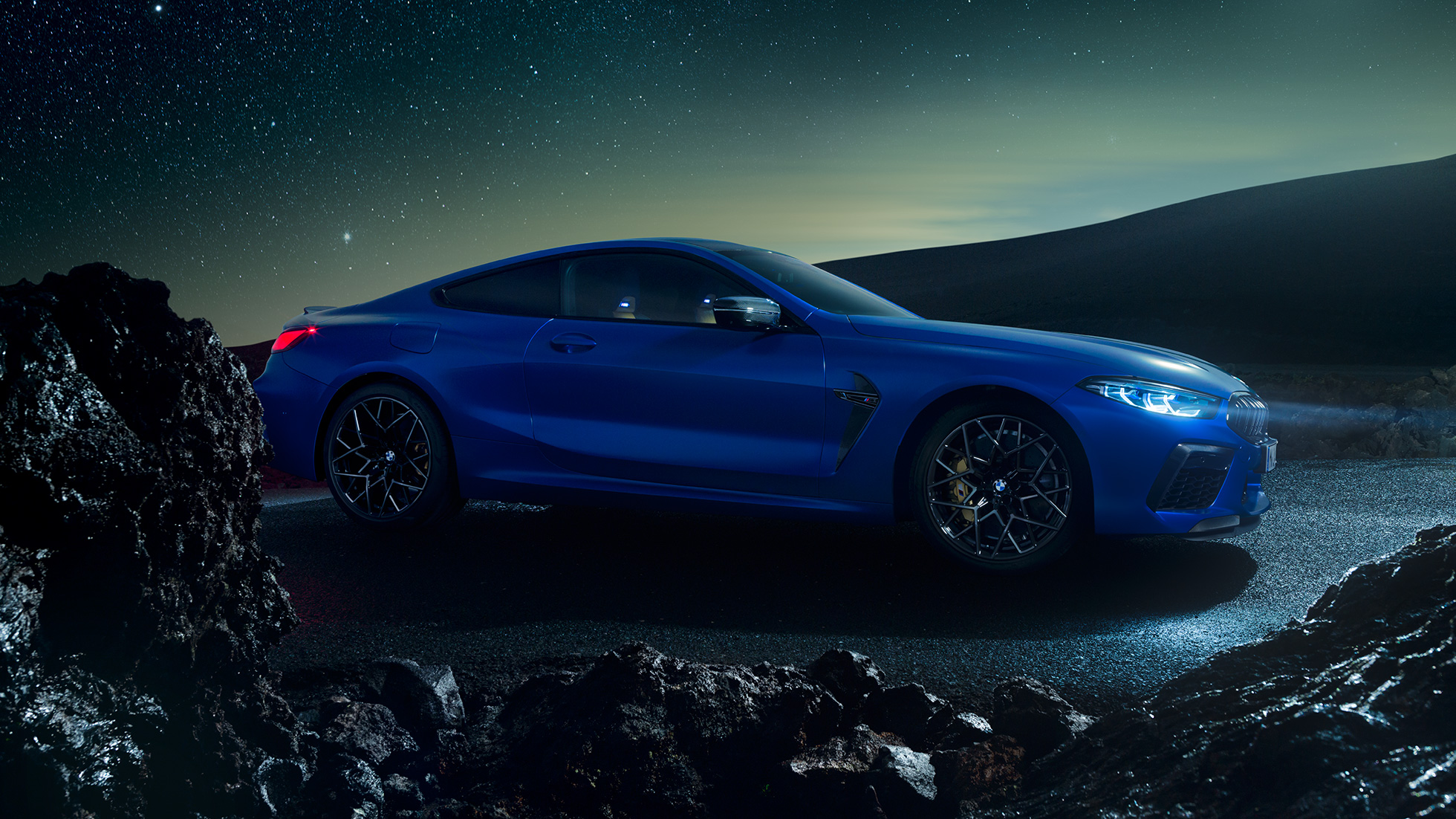 BMW M8 Competition Coupé, perspetiva lateral a três quartos. BMW M8 Competition Coupé na pintura azul Marina Bay metalizada, parado à noite, perspetiva lateral a três quartos.