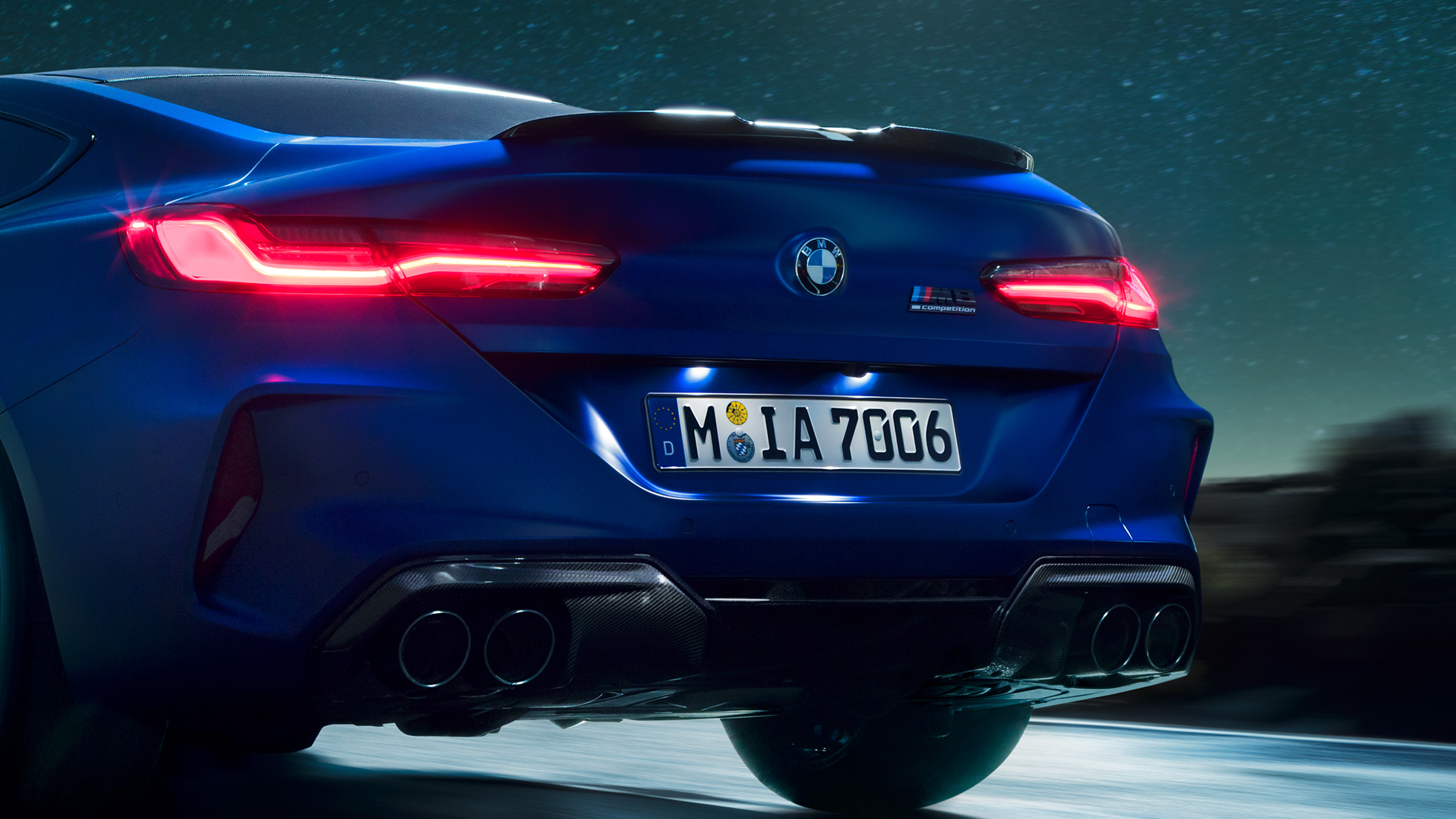 Difusor M em preto Carbon. BMW M8 Competition Coupé na pintura azul Marina Bay metalizada, grande plano da traseira, com o difusor M em preto Carbon à noite.