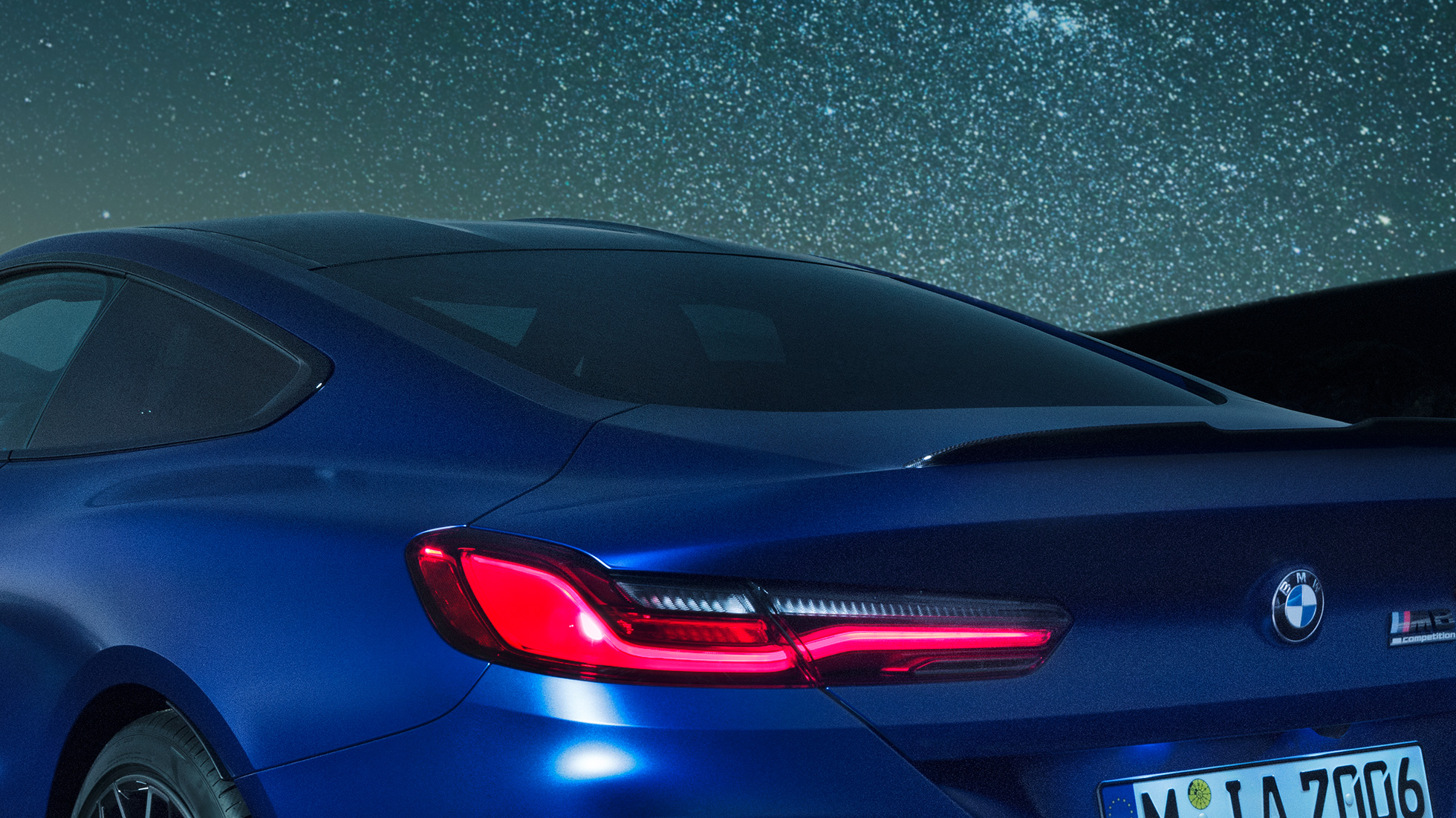 Spoiler traseiro M BMW M8 Competition Coupé na pintura azul Marina Bay metalizada, grande plano das linhas com spoiler traseiro M em carbono à noite.