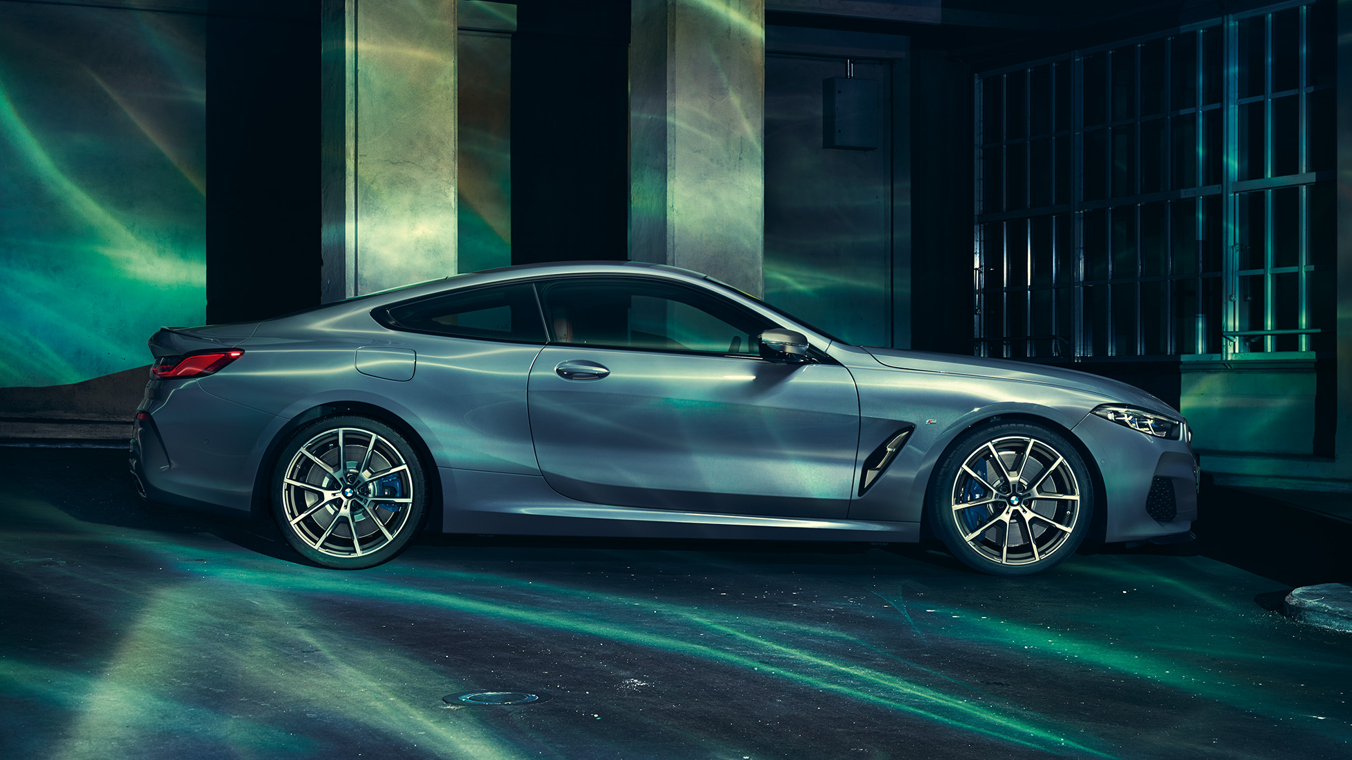 BMW M850i xDrive Coupé, perspetiva lateral. BMW M850i xDrive Coupé na pintura azul Barcelona metalizada, parado em frente a um edifício, perspetiva lateral.