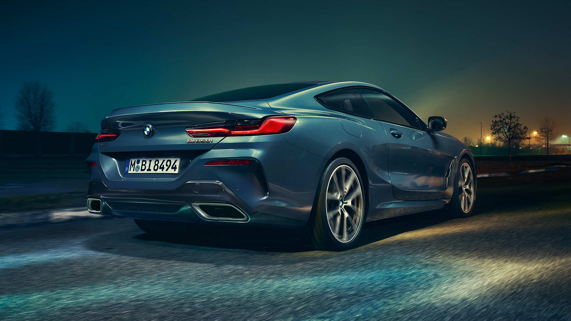 BMW M850i xDrive Coupé, perspetiva traseira. BMW M850i xDrive Coupé na pintura azul Barcelona metalizada, em movimento à noite, perspetiva traseira.