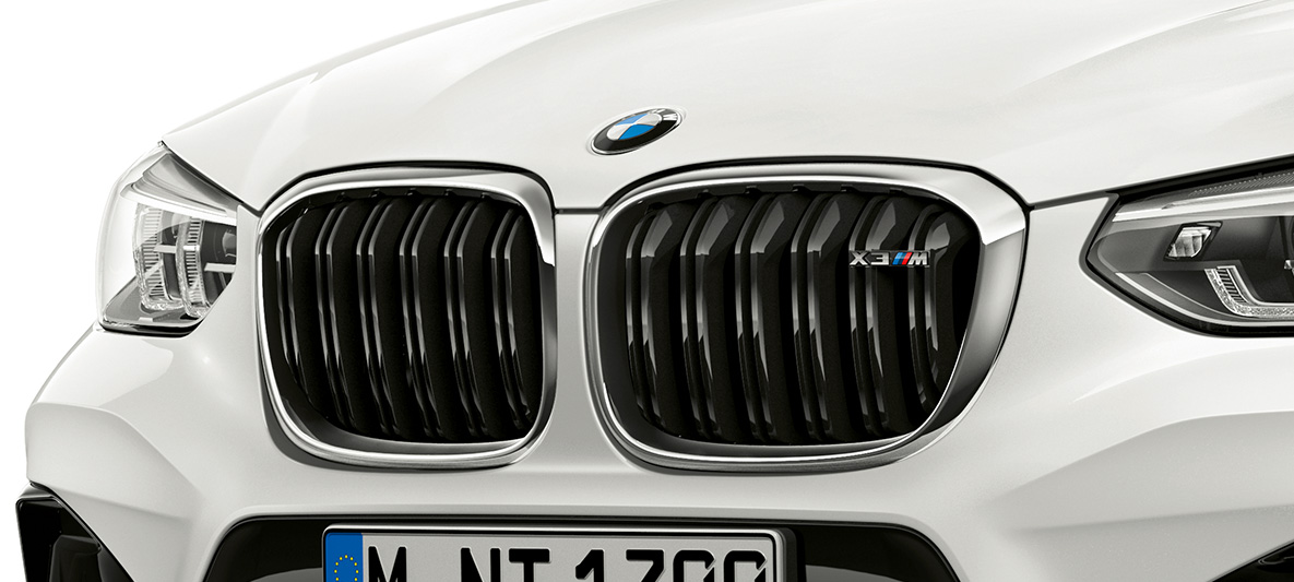 BMW X3 M, grelha M em forma de rim. BMW X3 M na pintura branco Alpine, exterior, dianteira, grelha M em forma de rim com realces em cromado e designação do modelo.