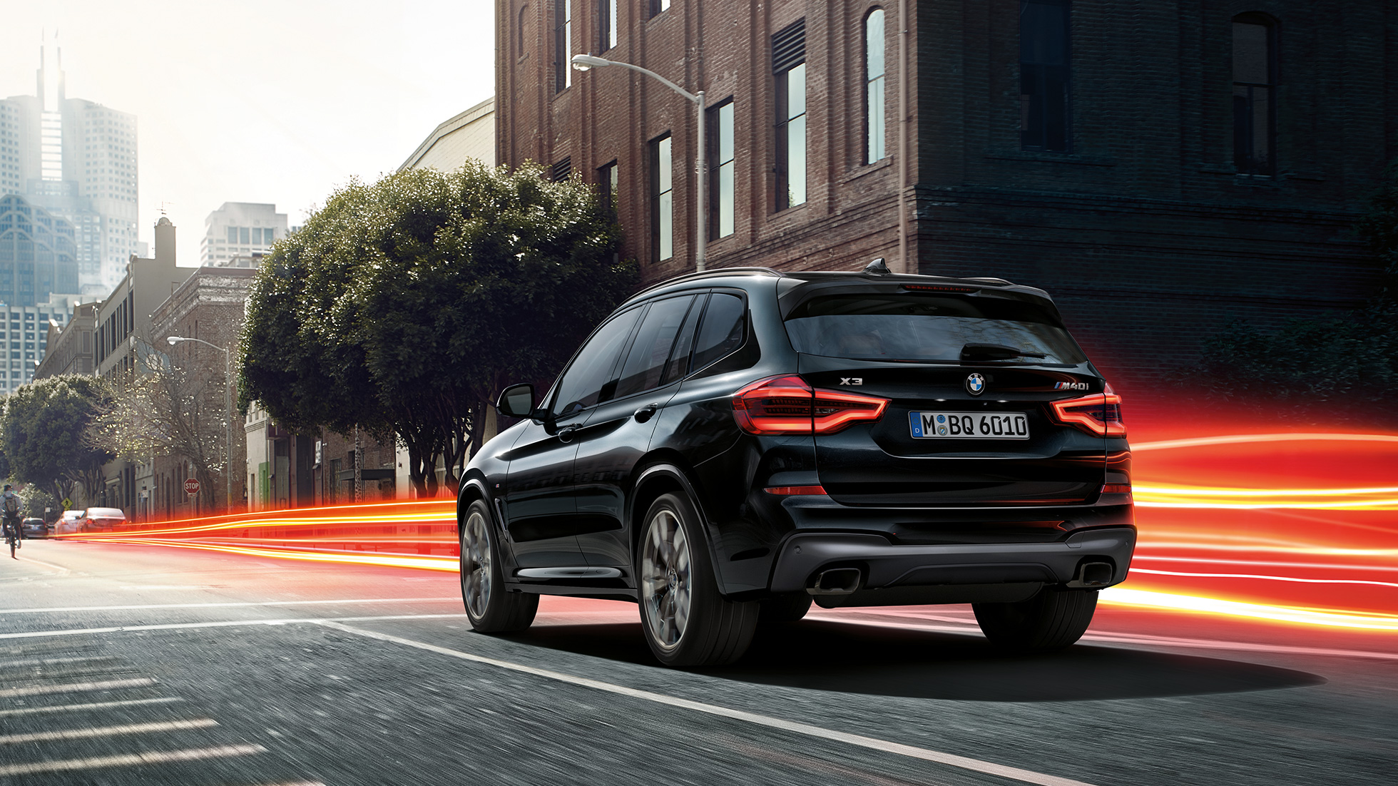 BMW X3 M40i, perspetiva traseira a três quartos. BMW X3 M40i na pintura preto Sapphire metalizada em movimento, exterior, perspetiva traseira a três quartos, em cenário urbano com faixas luminosas.