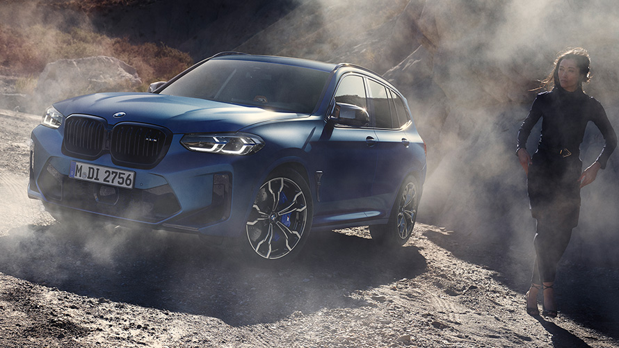 BMW X3 M Competition, F97, LCI, 2021, perspetiva frontal a três quartos, parado em piso empedrado BMW X3 M Competition, F97, LCI, atualização, 2021, cor exterior azul Frozen Marina Bay metalizada, perspetiva frontal a três quartos, parado em piso empedrado com um modelo feminino