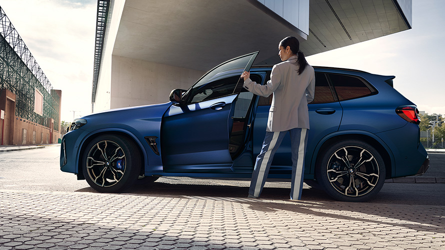 BMW X3 M Competition, F97, LCI, 2021, perspetiva lateral com a porta aberta e um modelo feminino BMW X3 M Competition, F97, LCI, atualização, 2021, cor exterior azul Frozen Marina Bay metalizada, perspetiva lateral com a porta aberta e um modelo feminino