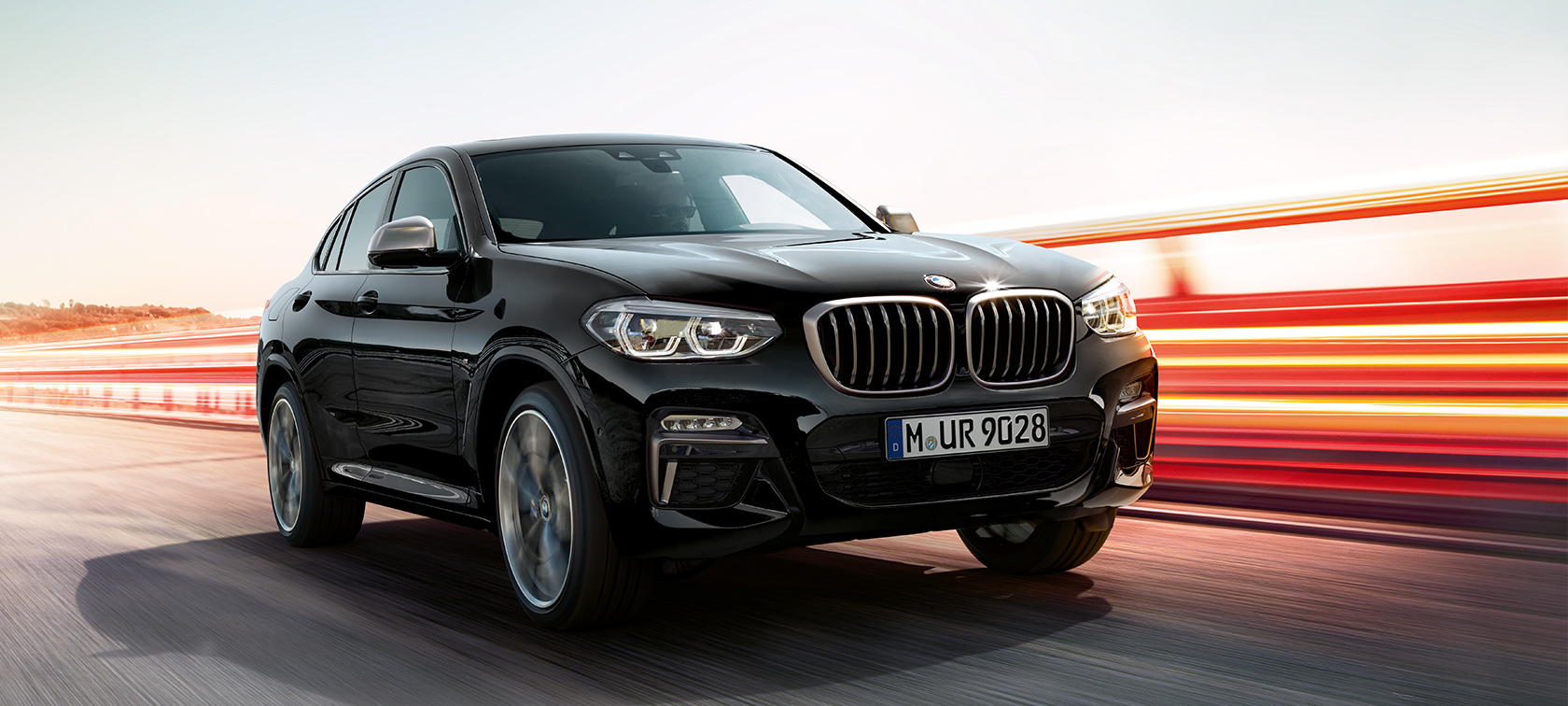 BMW X4 M40d, perspetiva frontal a três quartos, lado esquerdo. BMW X4 M40d na pintura preto Sapphire metalizada, exterior, perspetiva frontal a três quartos, lado esquerdo com faixas luminosas.