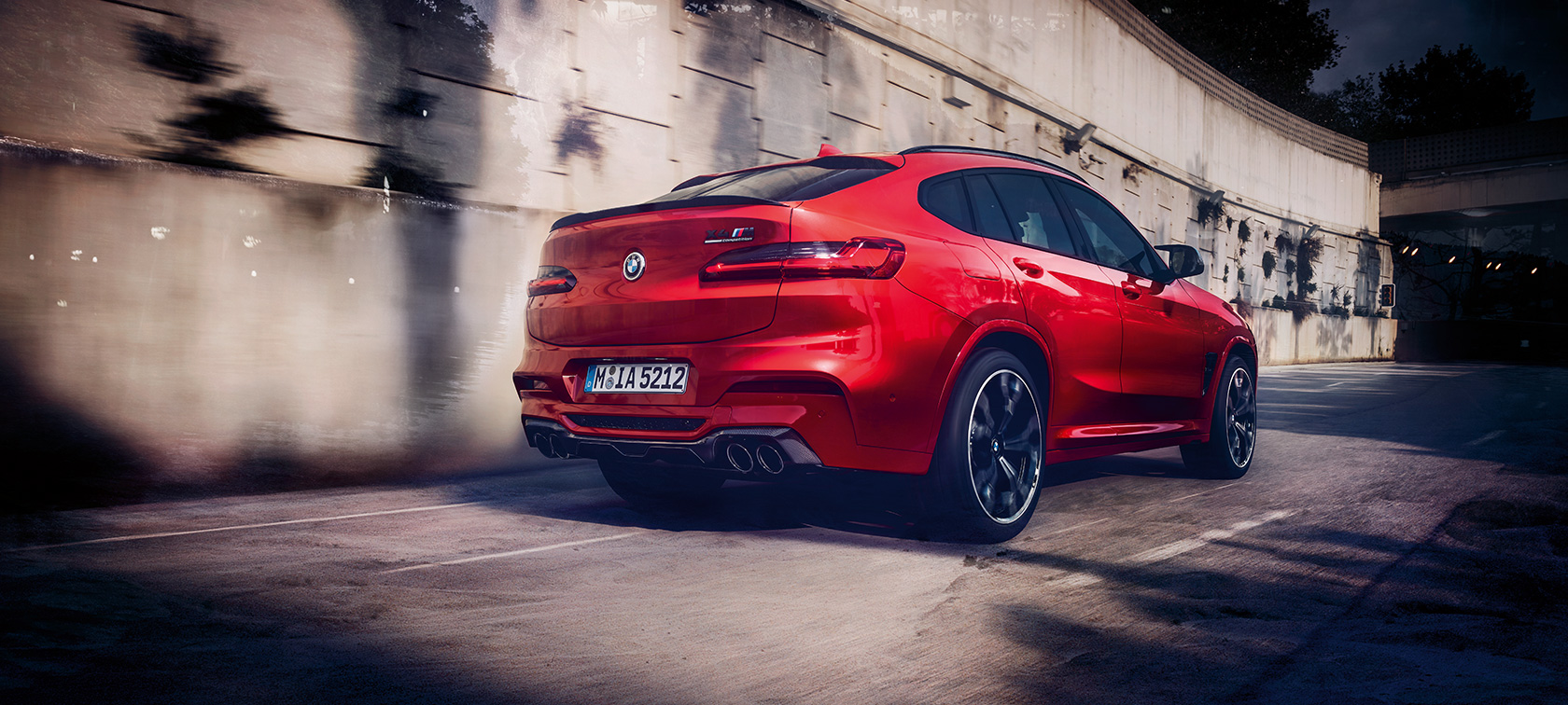 BMW X4 M Competition, perspetiva traseira a três quartos. BMW X4 M Competition na pintura vermelho Toronto metalizada em mvimento, exterior, perspetiva traseira a três quartos.