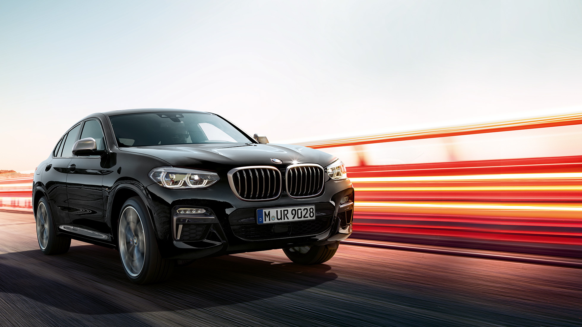 BMW X4 M40i, perspetiva traseira a três quartos. BMW X4 M40i em movimento, na pintura preto Sapphire metalizada, exterior, perspetiva traseira a três quartos, com faixas luminosas.
