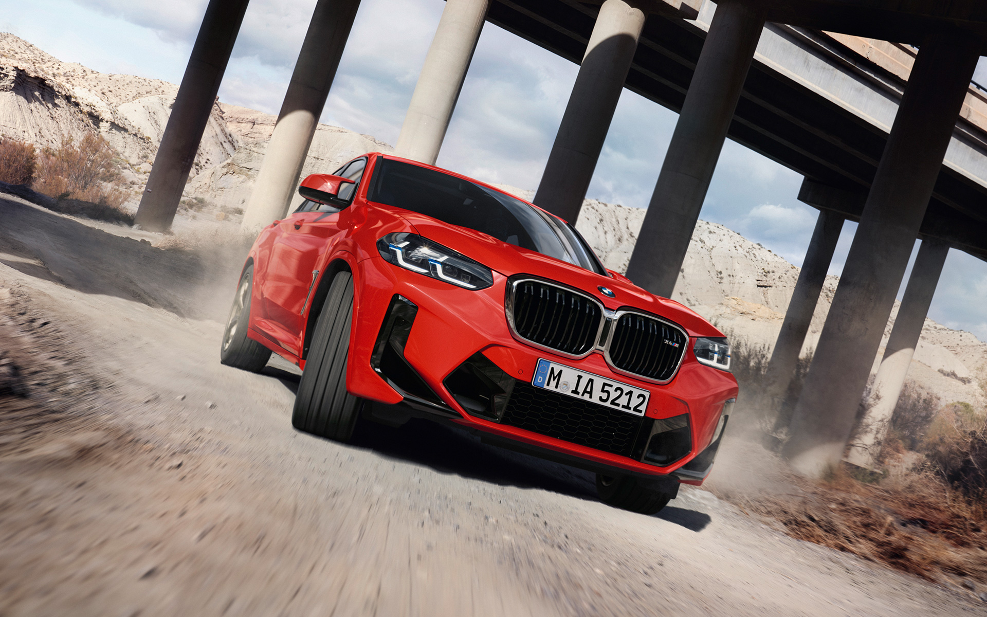 BMW X4 M, F98, LCI, atualização, 2021, cor exterior vermelho Toronto metalizada, perspetiva frontal a três quartos, em frente aos pilares de uma ponte