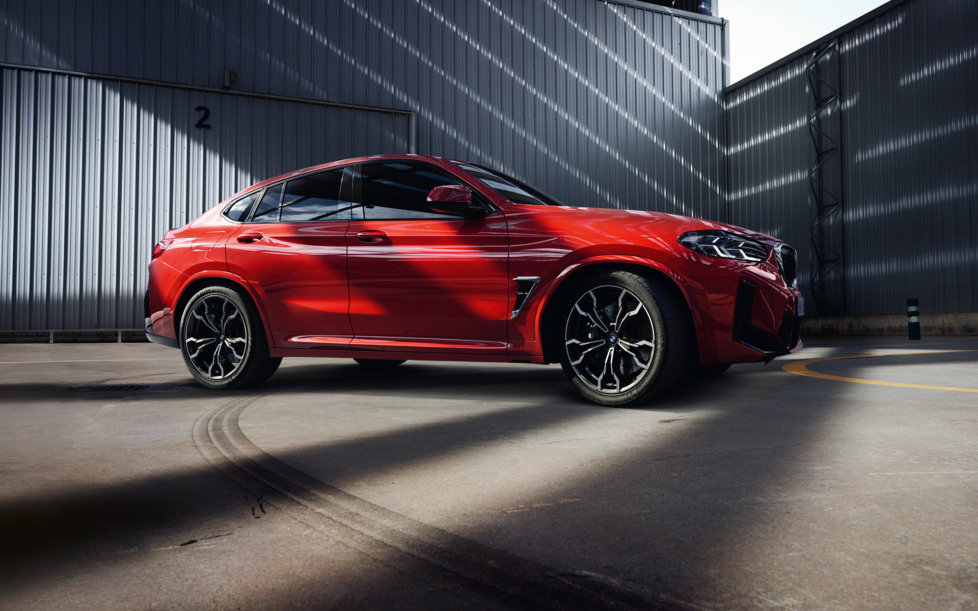BMW X4 M, F98, LCI, atualização, 2021, cor exterior vermelho Toronto metalizada, perspetiva lateral, em frente a um edifício de uma fábrica