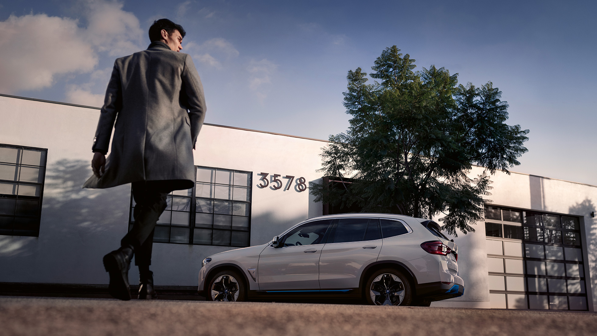 BMW iX3, G08, perspetiva frontal em frente a um edifício com um homem BMW iX3, G08, 2020, branco Mineral metalizado, perspetiva frontal em frente a um edifício com um homem