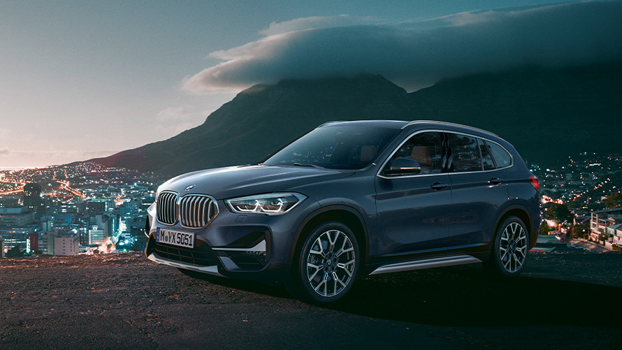 BMW X1, F48 segunda geração, perspetiva lateral a três quartos, parado em frente a uma cidade Modelos BMW X, BMW X1, F48 segunda geração, perspetiva lateral a três quartos, parado em frente a uma cidade