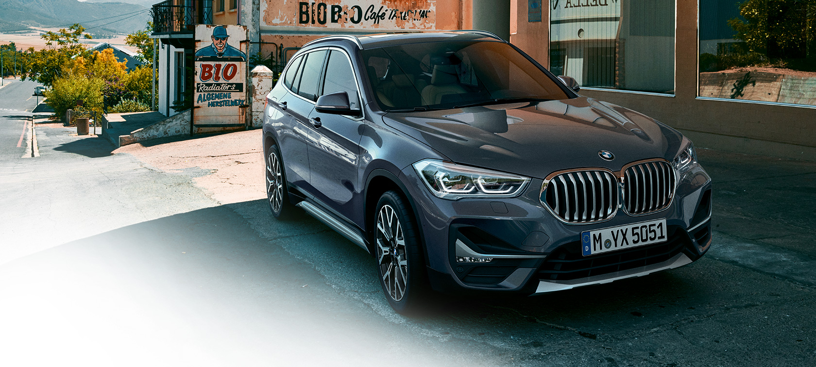 BMW X1, perspetiva frontal a três quartos. BMW X1, perspetiva frontal a três quartos, em frente a um cenário urbano.
