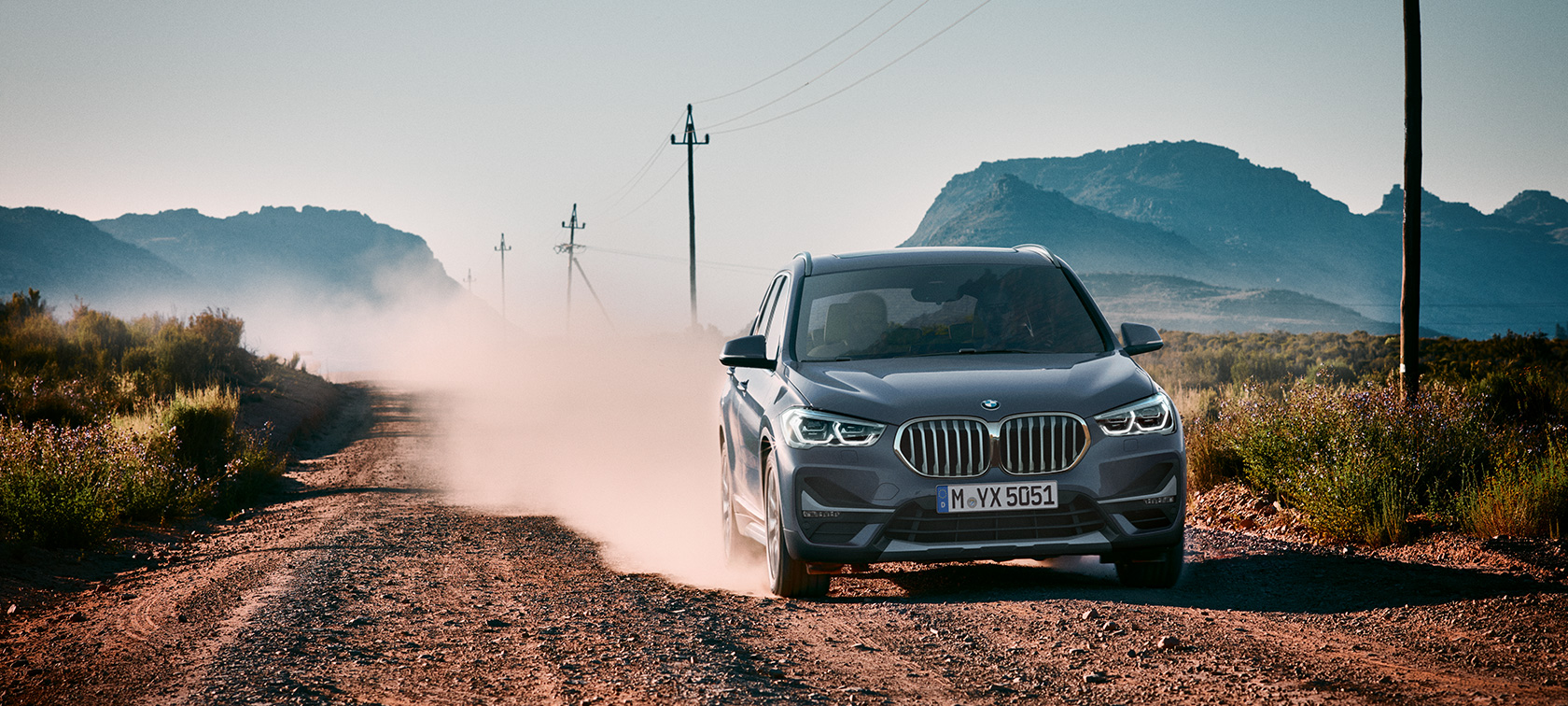 BMW X1, perspetiva traseira a três quartos. BMW X1, perspetiva traseira a três quartos, condução em frente a um cenário de montanha.