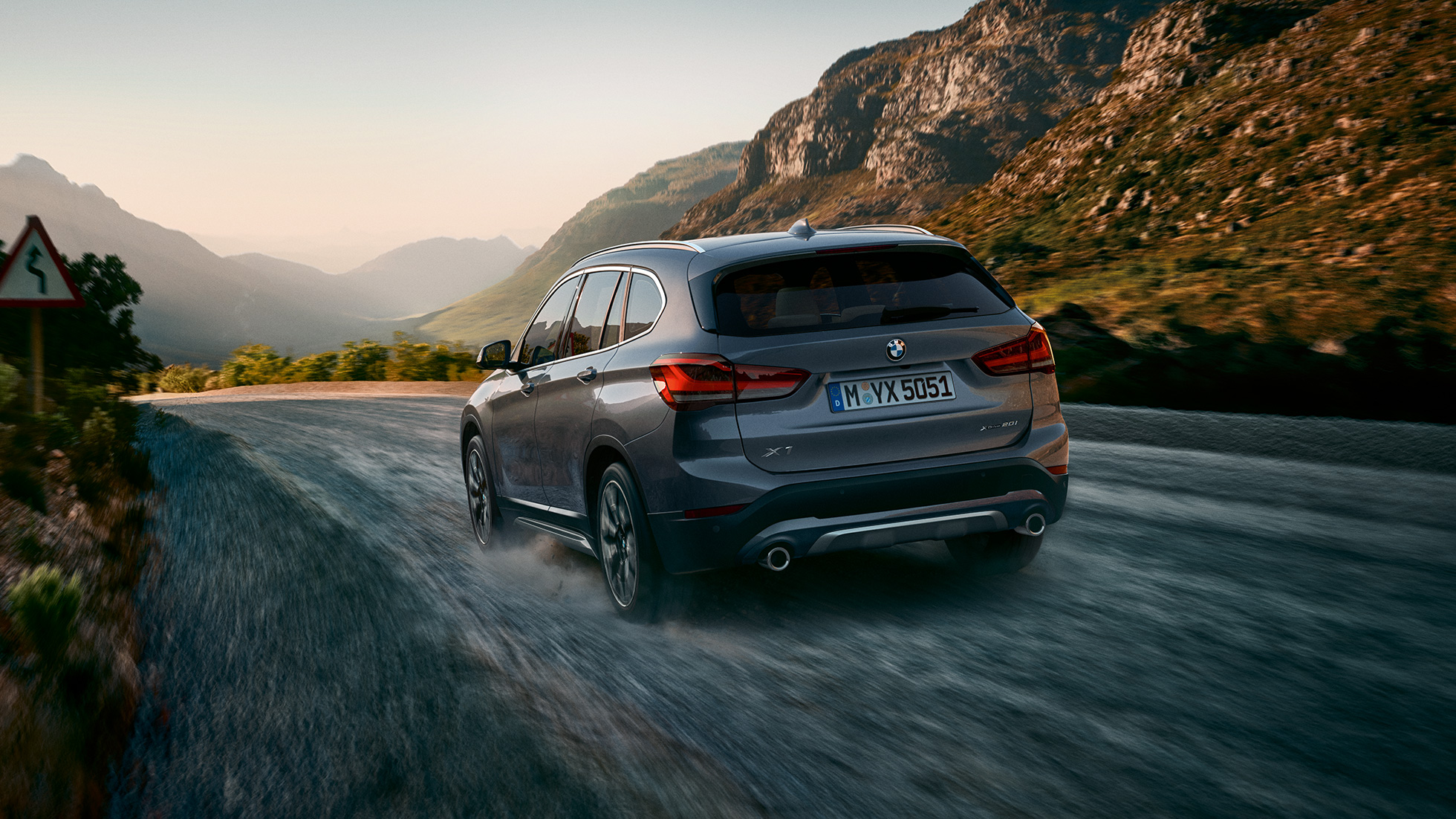 BMW X1, perspetiva traseira a três quartos. BMW X1, perspetiva traseira a três quartos, condução em frente a um cenário de montanha.