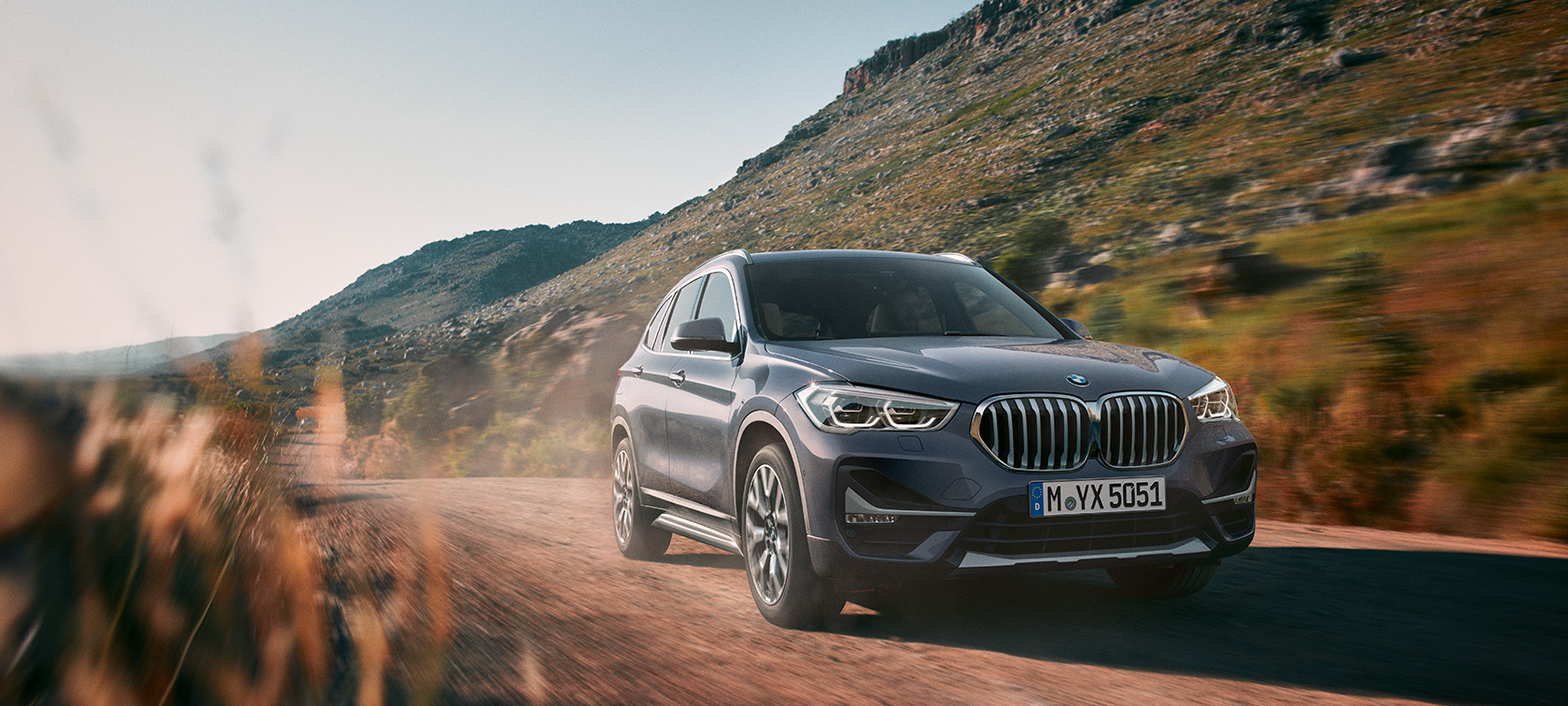 BMW X1, perspetiva frontal a três quartos. BMW X1, perspetiva frontal a três quartos, condução em frente a um cenário de montanha.