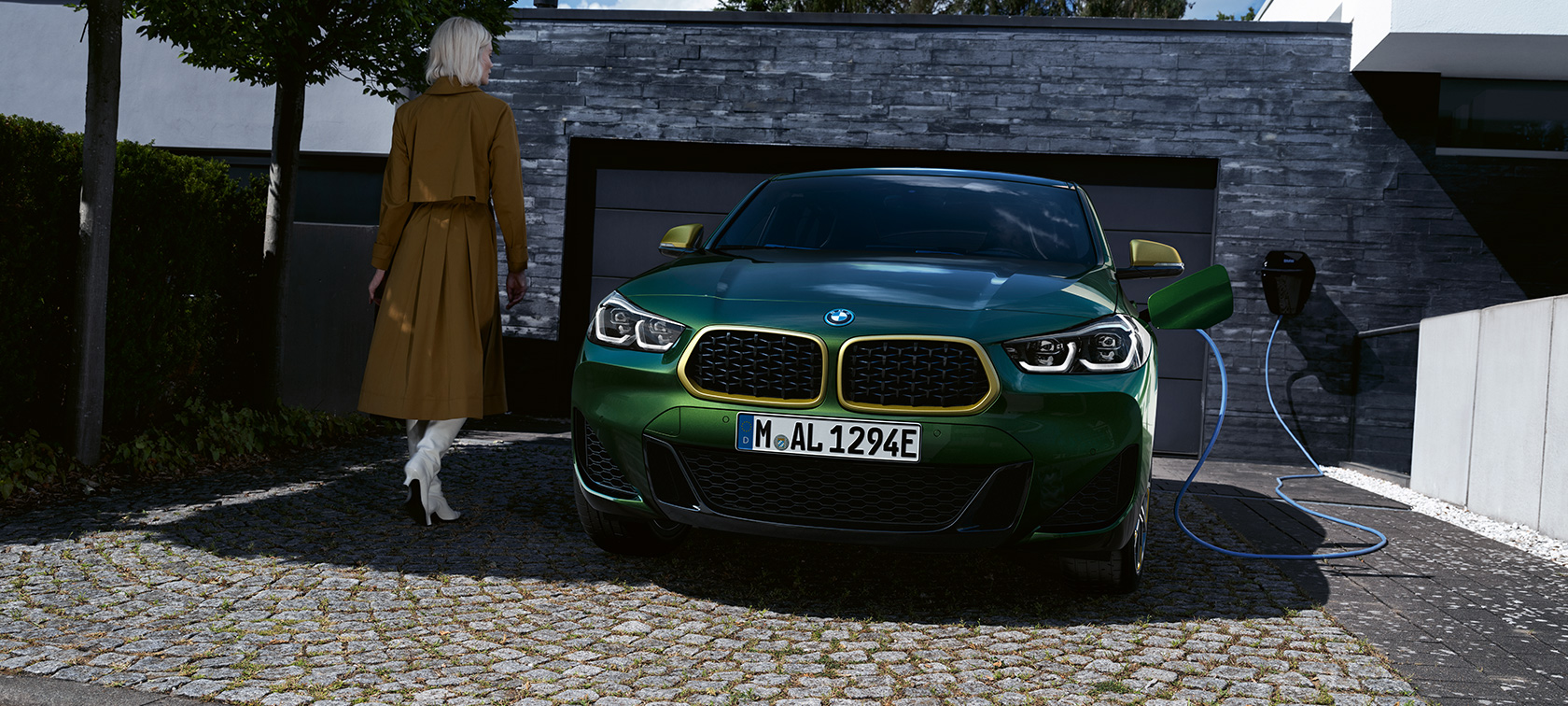 Perspetiva frontal, BMW X2, F39, pintura verde Sanremo metalizada Perspetiva frontal, a carregar com um modelo à esquerda, BMW X2, F39, pintura verde Sanremo metalizada