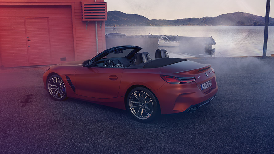 Perspetiva traseira do BMW Z4 First Edition em laranja Perspetiva traseira do BMW Z4 First Edition em frente de uma casa vermelha, na praia