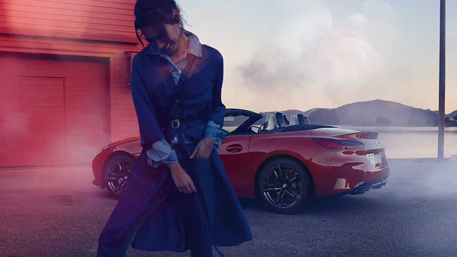 BMW Z4 M40i Roadster G29 com capota aberta BMW Z4 M40i Roadster G29, perspetiva traseira a três quartos, com a capota aberta e uma mulher em primeiro plano