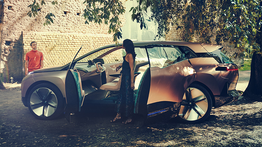 BMW Vision iNEXT de lado BMW Vision iNEXT de lado com mulher em frente a portas abertas e homem em segundo plano