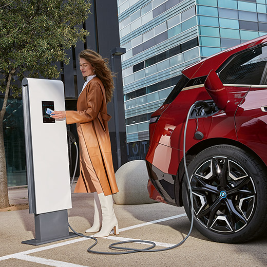 BMW iX, i20, num posto de carregamento, mulher com o cartão de carregamento BMW