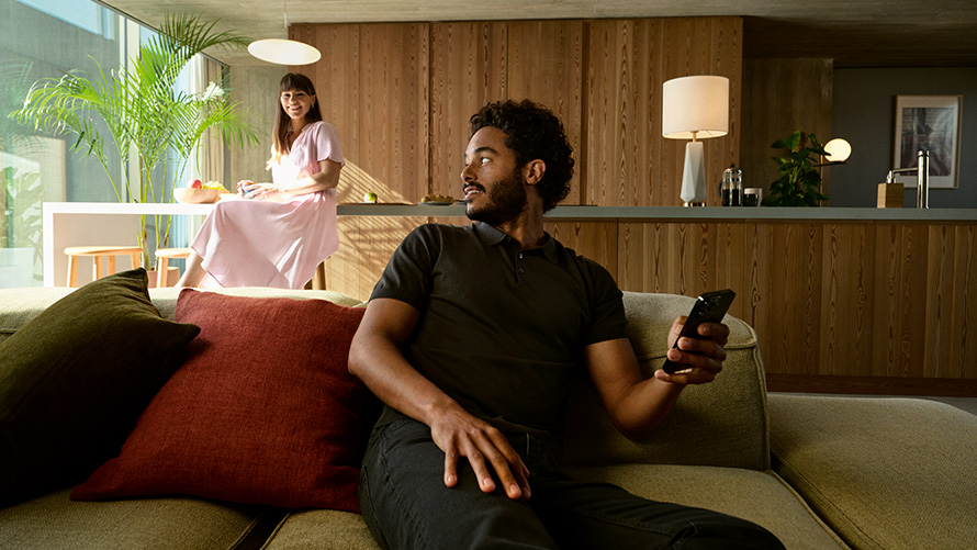 Partilhar chave digital BMW Chave digital BMW, homem com um smartphone na mão sentado no sofá com uma mulher na imagem de fundo