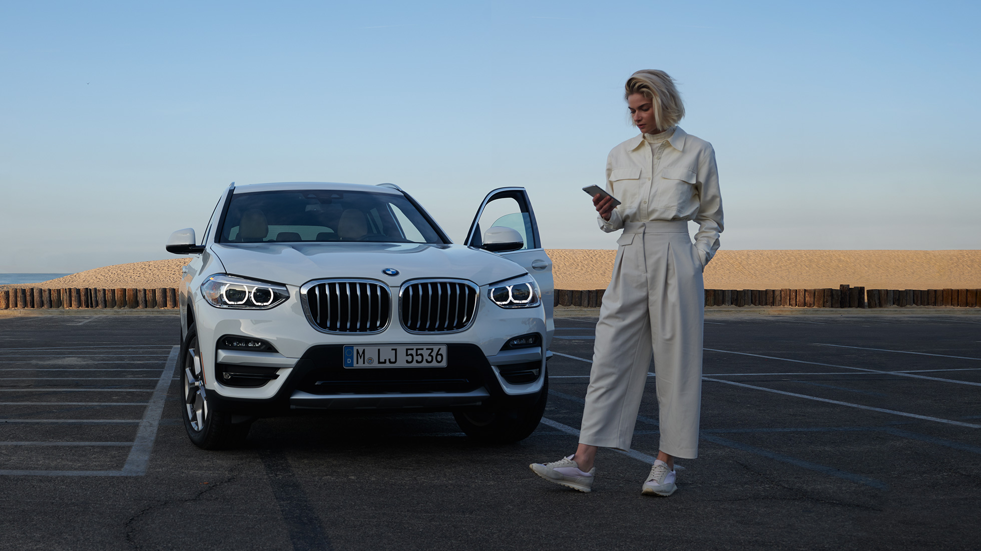 Mulher utiliza a aplicação My BMW num smartphone Mulher utiliza a aplicação My BMW integrada nas tecnologias BMW ConnectedDrive no smartphone, em frente a um BMW X5 em branco