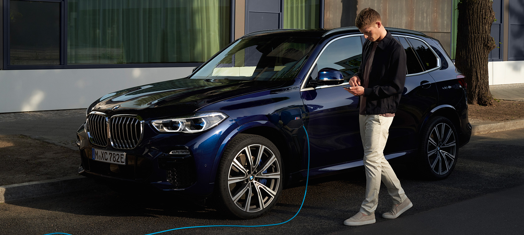 Homem a utilizar a aplicação My BMW no smartphone Homem a utilizar a aplicação My BMW do BMW ConnectedDrive no Smartphone enquanto carrega o seu BMW X5 híbrido Plug-in