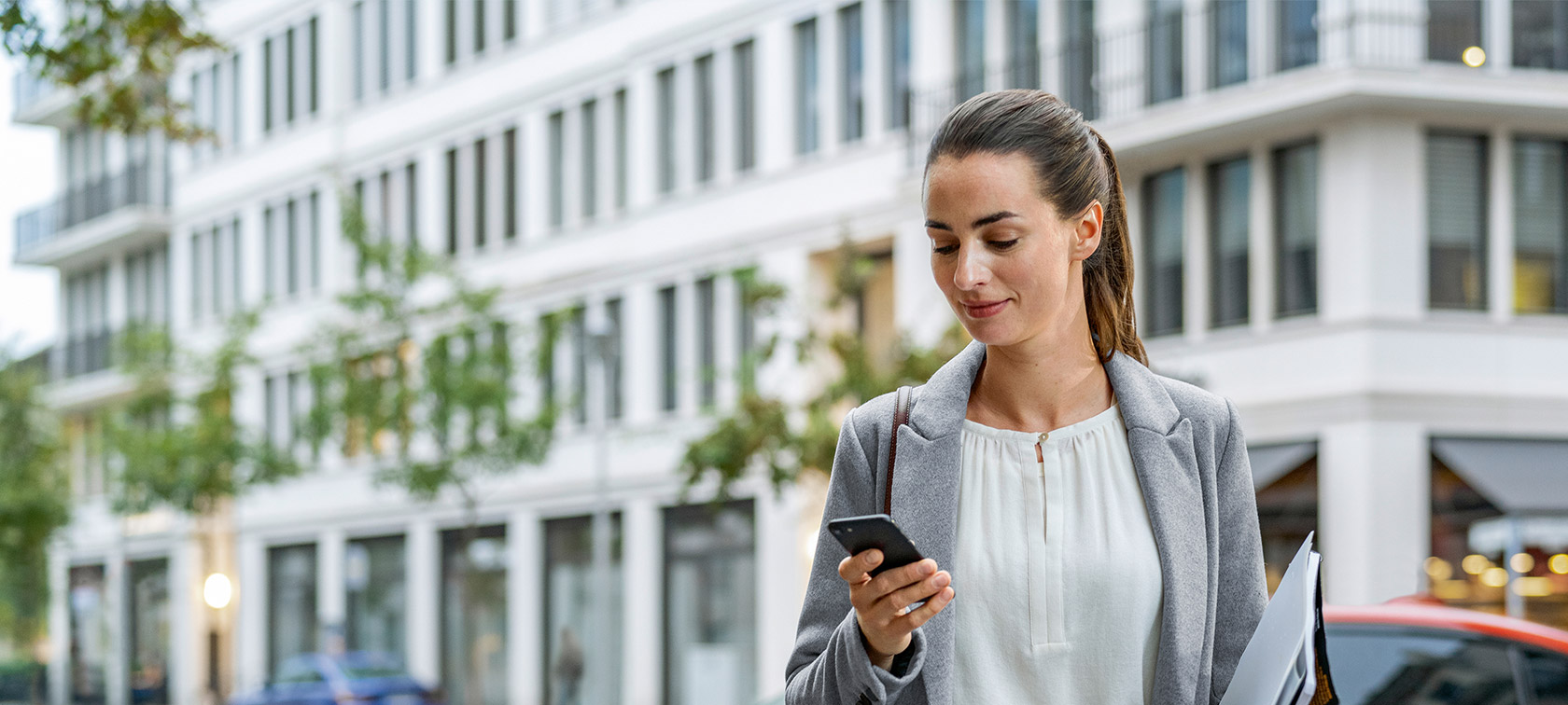 Mulher à frente de um edifício a olhar para o seu smartphone Atualização de software à distância, mulher à frente de um edifício a olhar para o seu smartphone