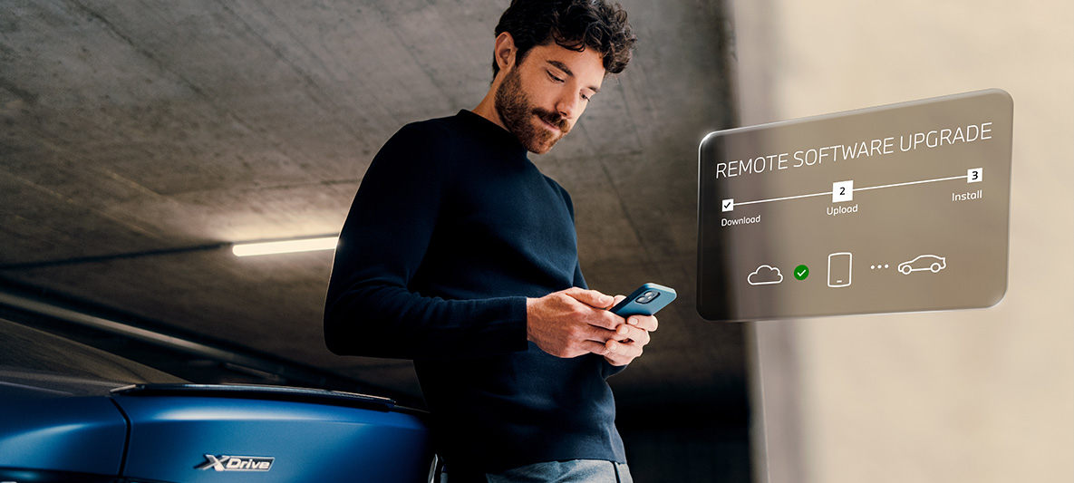 Homem encostado à traseira de um BMW a olhar para o seu smartphone Atualização de software à distância, homem encostado à traseira de um BMW a olhar para o seu smartphone