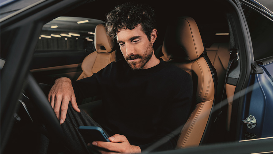 Homem sentado num BMW Homem sentado num BMW e a olhar para o seu smartphone