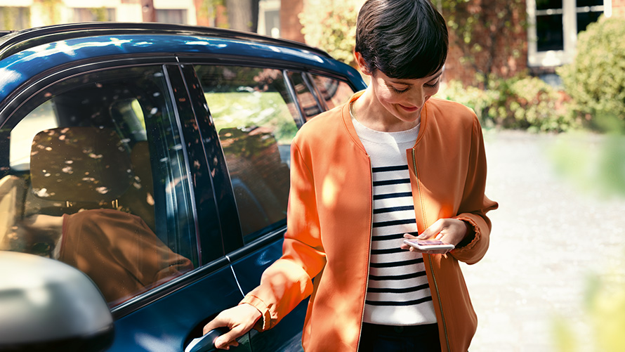 BMW TeleServices Mulher com um smartphone ao lado da porta do seu BMW