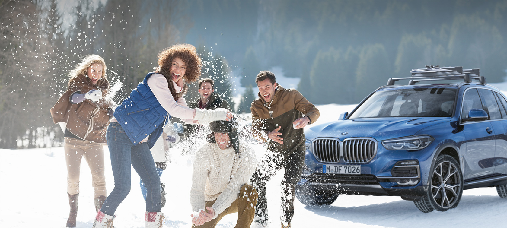 Acessórios Originais BMW e BMW Service para outono e inverno Homem e mulher a rirem, na neve, em frente a um BMW
