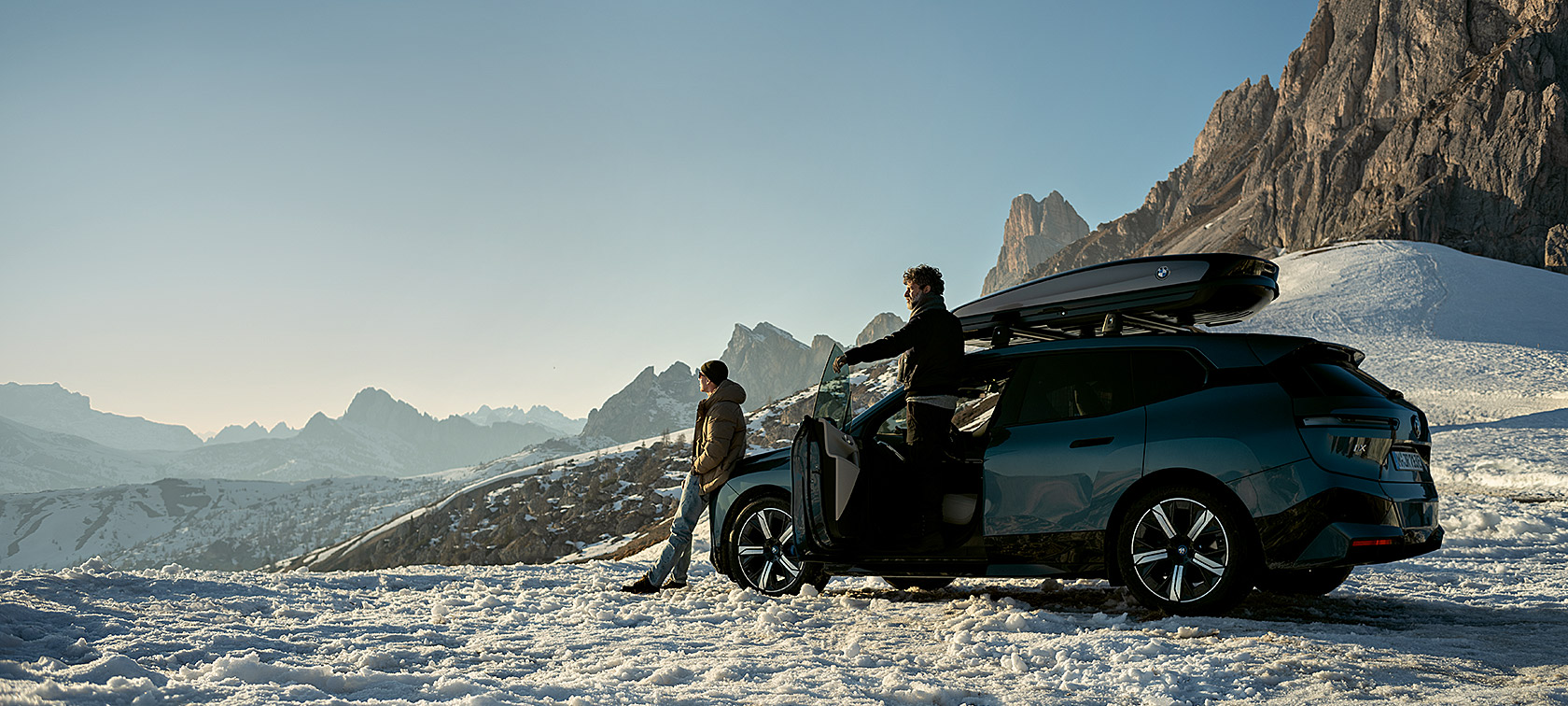 Acessórios Originais BMW e BMW Service para outono e inverno Homem com um BMW iX num cenário de neve