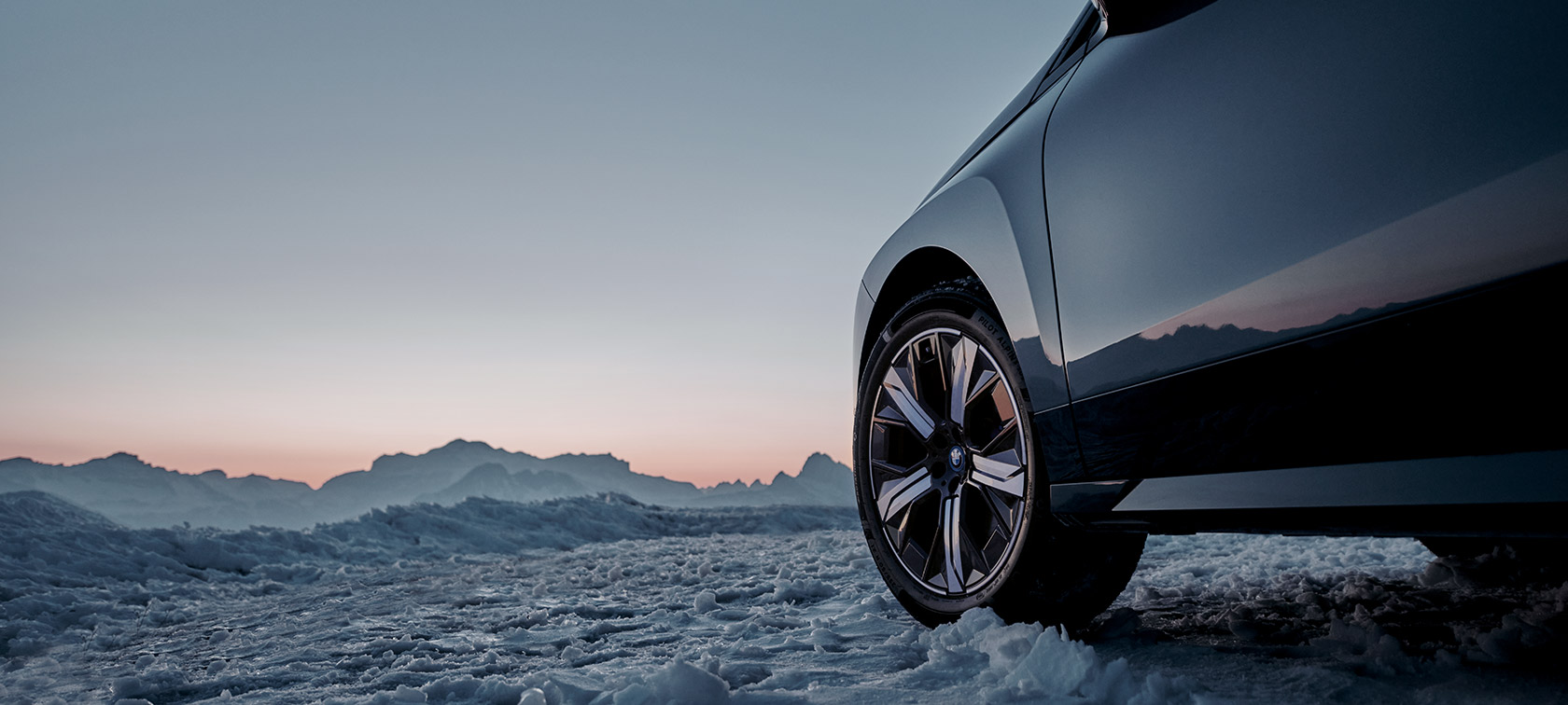 Jantes Originais BMW do BMW iX (I20) na neve em frente a montanhas Jantes Originais BMW do BMW iX (I20) na neve em frente a montanhas