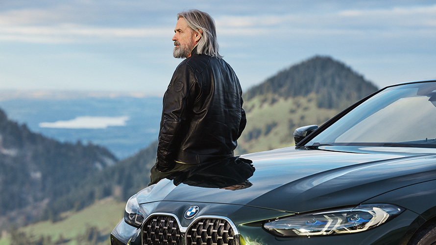 Homem junto a um BMW em frente a um cenário de montanha Acessórios primavera/verão BMW, homem junto a um BMW em frente a um cenário de montanha