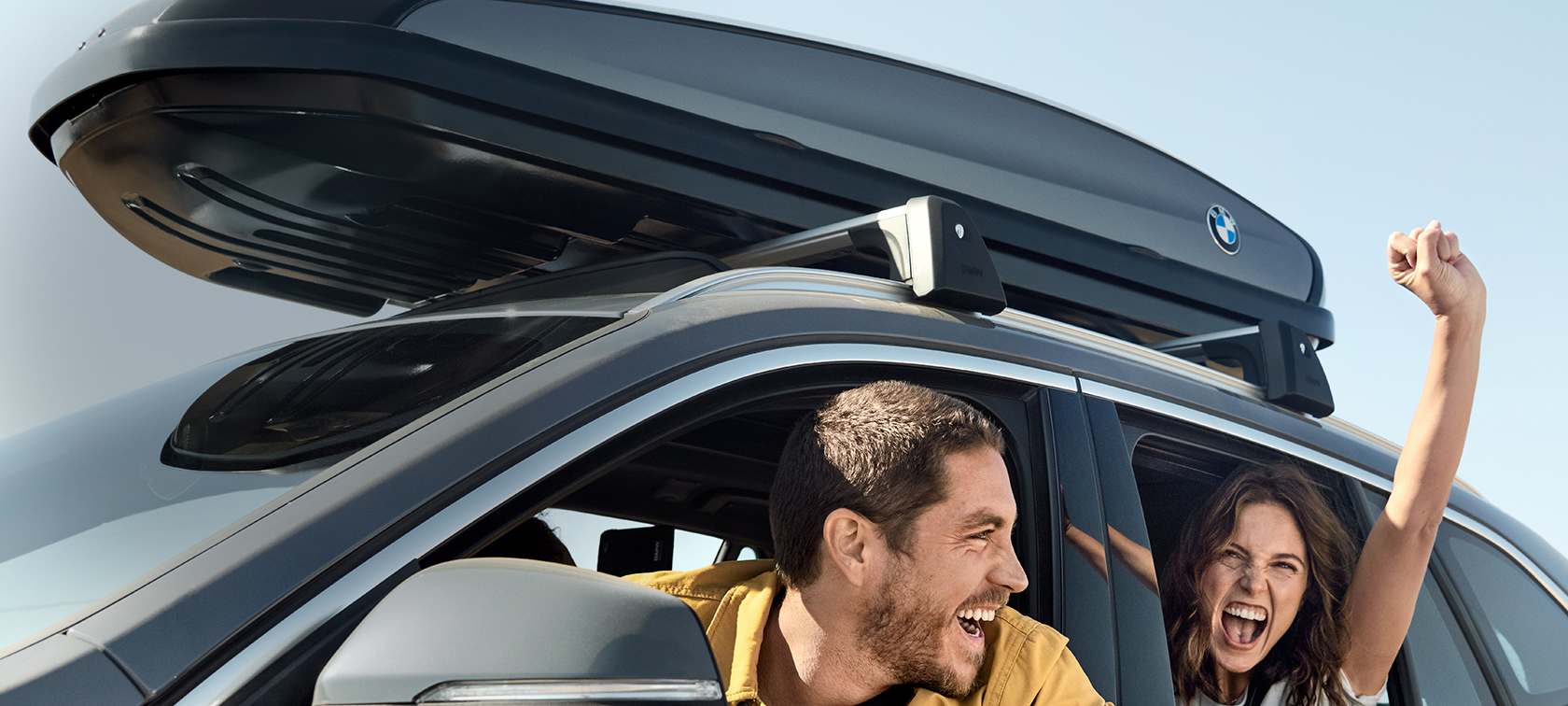 Casal feliz num BMW X1 com as ofertas BMW para o verão Casal feliz num BMW X1 em cinza Mineral equipado com as ofertas BMW para o verão, sob um céu azul, vista lateral a três quartos