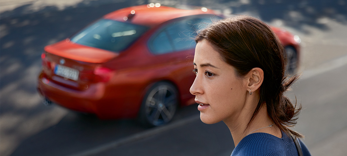 Uma mulher a olhar para a distância. Um BMW passa atrás dela. Uma mulher a olhar para a distância. Um BMW passa atrás dela.