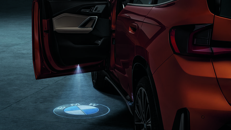 Acessórios Originais BMW X BMW X1 com porta dianteira da esquerda aberta e símbolo da BMW projetado no chão.