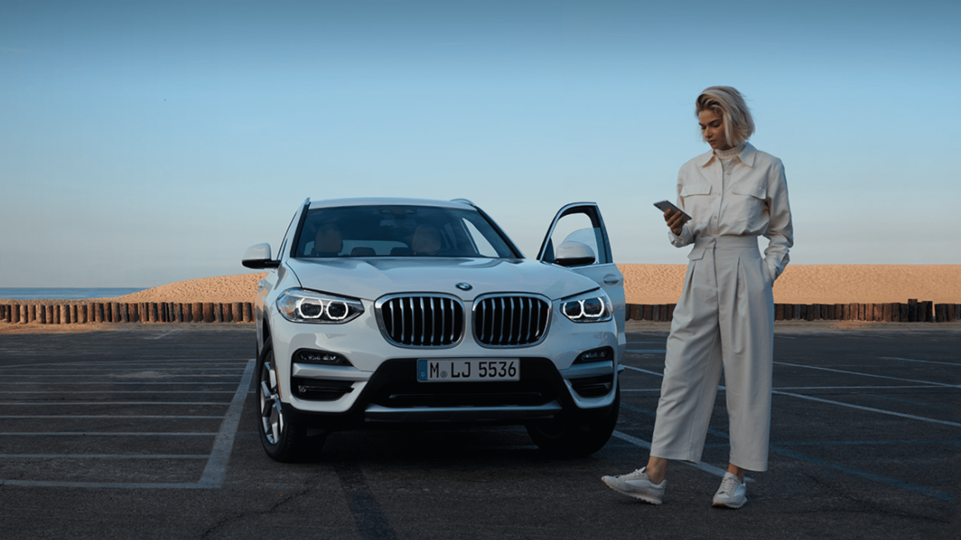 Escolha e Agendamento BMW Mulher a mexer no telemóvel ao pé de um BMW.