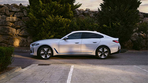 BMW i4, de cor branca, estacionado com árvores de fundo.