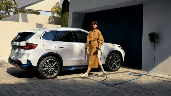 Mulher vestida de vestido beje encaminha-se para carregar o BMW iX1 através da Wallbox.